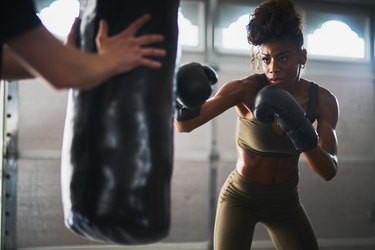 african woman boxing with punching bag in garage gym