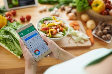 an overhead photo of a person using a calorie counter app on their phone with a salad in the background on a wooden cutting board