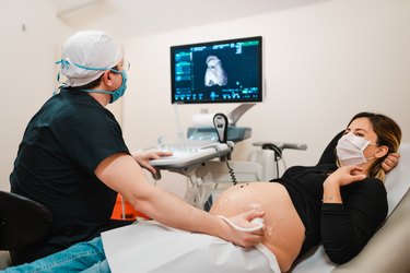 Pregnant woman wearing face mask watching her baby on the ultrasound
