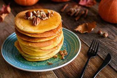 A stack of pumpkin pancakes on a light blue plate, topped with walnuts