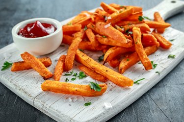 Healthy Homemade Baked Orange Sweet Potato Fries with ketchup, salt, pepper on white wooden board