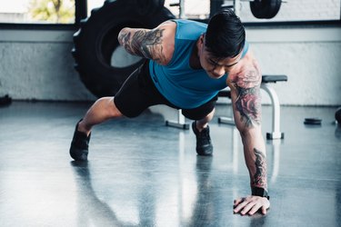 young sportsman doing one-arm plank exercise at gym