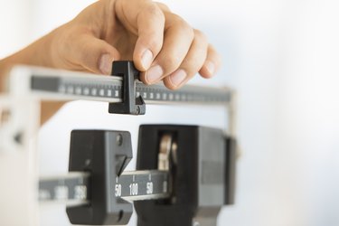 A hand adjusting the weight on a scale to represent obesity