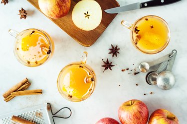 Mugs of mulled apple cider, a drink with many health benefits, with spices on a table.