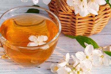 篮子里的花山梅花somewhere called jasmine or mock orange and Cup with fragrant jasmine tea on a white wooden tray outdoors in summer