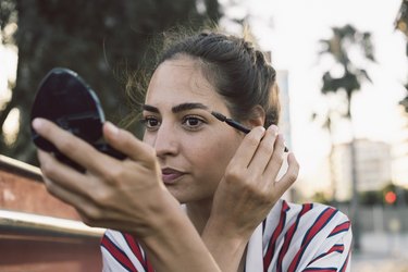 Young woman applying mascara with a compact mirror