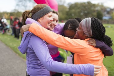 Happy female runners hugging at  charity race finish line, celebrating