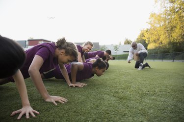 Physical education teacher encouraging students doing push-ups