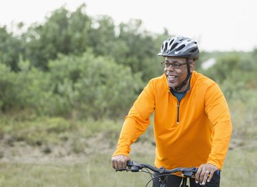 black man with glasses and helmet in orange pullover riding bike in park