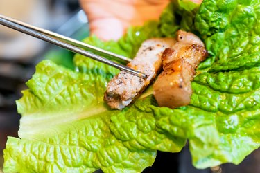 Pan-fried cooked black pork meal in Korea restaurant, fresh delicious korean food cuisine on iron plate with lettuce, close up, copy space, lifestyle