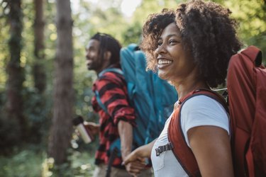 a couple smiling while holding hands and hiking outside, as a form of self-care