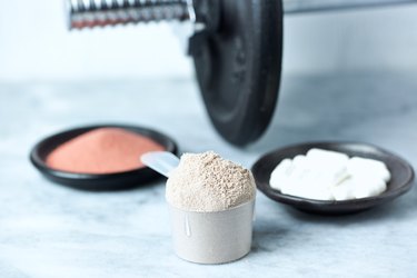 Scoop of Whey Protein, Beta-alanine capsules, Creatine Powder and a dumbbell in background. Sport nutrition. Stone / Wooden background. Copy space