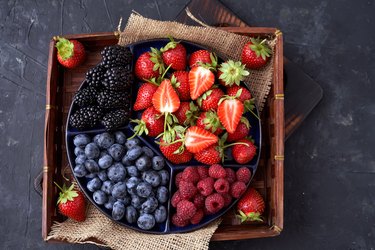 Strawberries, raspberries, blueberries, blackberries on a separate dish close-up on a solid concrete background. Healthy eating Vegan food. View from above