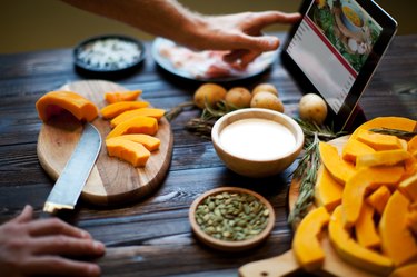 A man's hands cutting up vegetables while reading a recipe from a tablet