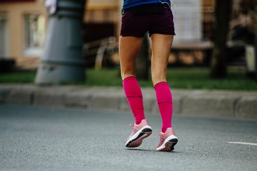 The bottom half of a person from behind, wearing bright pink knee-high compression socks and black shorts