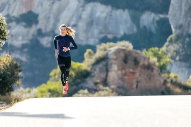 Sporty young woman running on mountain road in beautiful nature.
