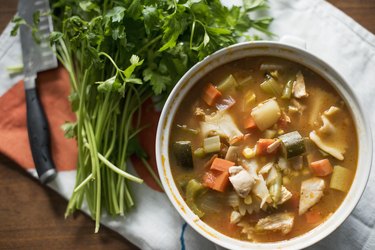 一碗蔬菜炖肉和一堆新鲜香草放在桌上。