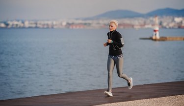 Side view of young sportswoman running outdoors on beach.