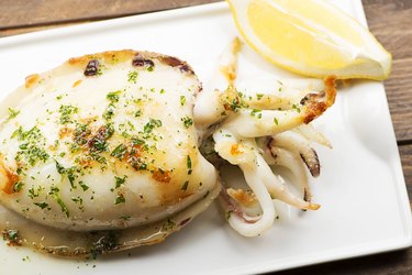 Close-up of iron-rich cuttlefish with garlic and parsley and lemon on white plate on wooden table