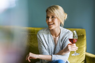 A smiling woman holding a glass of red wine and sitting on a green sofa