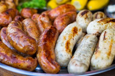 Fresh sausage and hot dogs grilling outdoors on a gas barbecue grill.