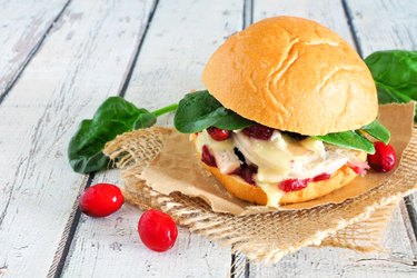 Roasted turkey sandwich with cranberry sauce and cheese, close up on white wood