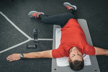 Sporty man stretching back before gym workout indoor on mat