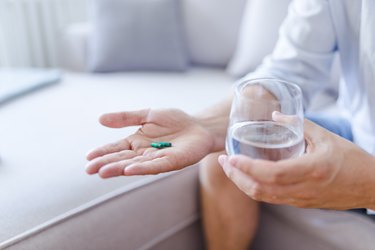 a close up of a person holding a keratin pill in one hand and a glass of water in the other hand