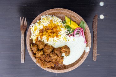 Indian food with lamb stew with rice and mango served in plastic plate with plastic fork and knife at food market