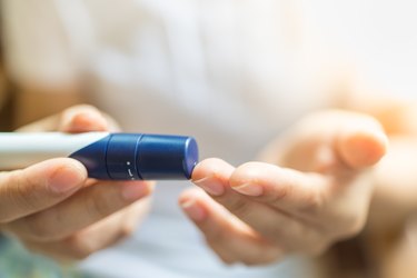 Woman using lancet on finger to check dangerous blood sugar levels with glucose monitor