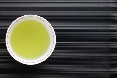 Top view of a teacup of fat-burn cleanse green tea on black striped background to show if matcha burns fat and if green tea does help with weight loss