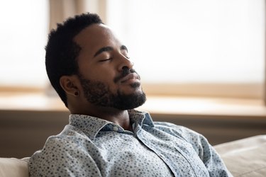 Tranquil young Black man with eyes closed breathing on couch