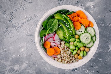 Vegan Buddha bowl salad with spinach, quinoa, roasted chickpeas, grilled chicken, avocado, edamame beans, cucumbers, sesame and pumpkin seeds.