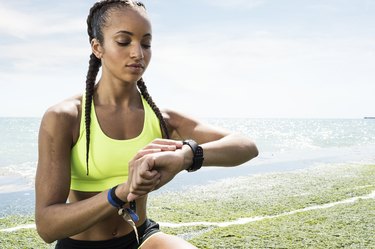 Young woman beside sea, wearing sports clothing, looking at activity tracker