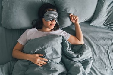 person sleeping in eye patch in grey bed.