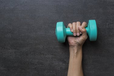 woman hand holding green dumbbell on black background
