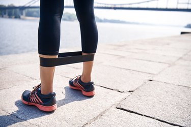 Cropped photo young sportive woman uses resistance band for exercising outdoors