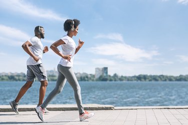 Smiling Afro Spouses Jogging Along River Bank In City