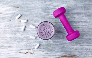 Glass of Protein Shake with milk and blueberries. BCAA amino acids and a violet dumbbell in background. Sport nutrition. Rustic wooden background. Top view. Copy space.