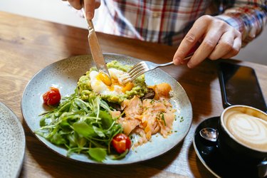 Man eating avocado toast with egg, salmon and arugula salad for brunch at a restaurant