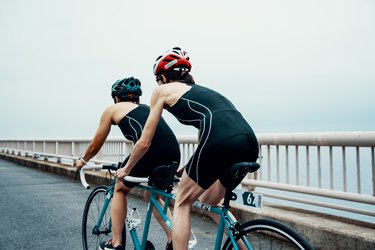 Visually impaired female triathlete training together with her guide and coach on a tandem bicycle