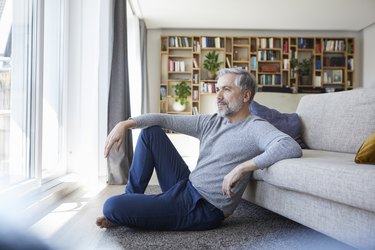 Mature man sitting on floor of his living room looking out of window