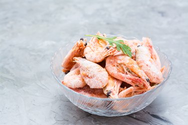 Group of frozen shrimp and a leaf of arugula in a glass bowl