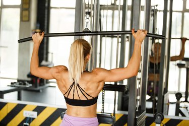 Fit female doing rear lat pull-down under supervision of her