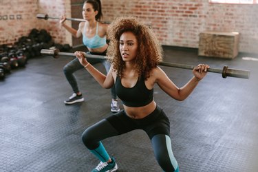 Two females workout in gym with barbell