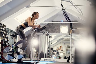 Young woman training, pedalling exercise bike in gym