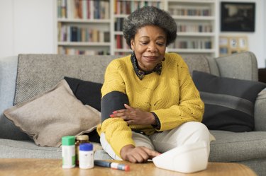 Woman sitting on a couch wearing blood pressure cuff with medications