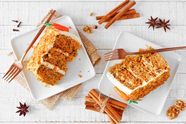 Two slices of homemade carrot cake with cream cheese frosting, top view table scene over white wood