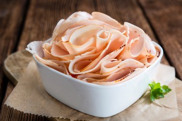 Sliced chicken breast in white dish on wooden table.