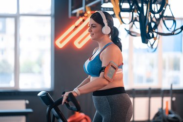 Woman cycling in gym and listening to music in earphones